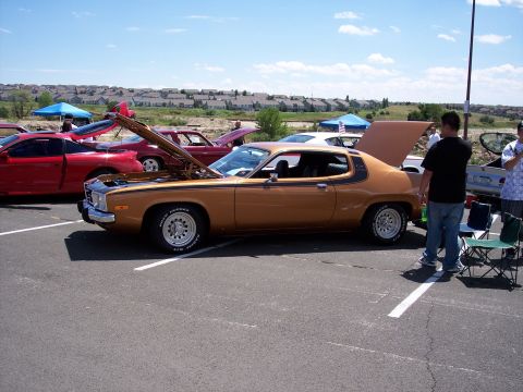1972 Ford Ranchero - A gold 1974 Plymouth Gran Fury coupe is displayed with its hood and trunk open at an outdoor car show.