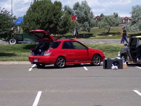 1972 Ford Ranchero - A red Subaru Impreza WRX wagon is parked with its trunk open, next to another vehicle and audio equipment.