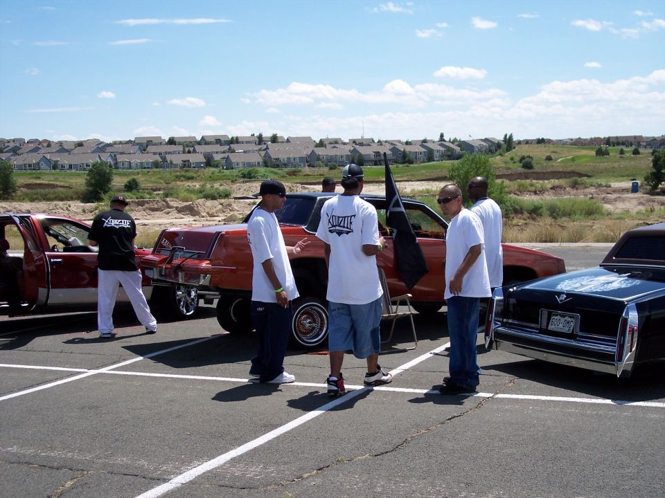 Group of men gathered around several lowrider cars parked in a lot
