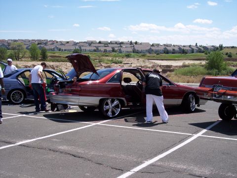 1972 Ford Ranchero - People gathered around customized cars in a parking lot on a sunny day with houses in the background.