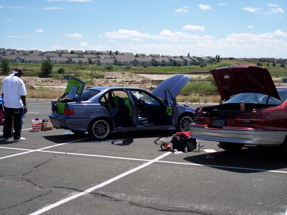 Two cars, a blue sedan and a red sedan, parked in a lot with hoods and trunks open