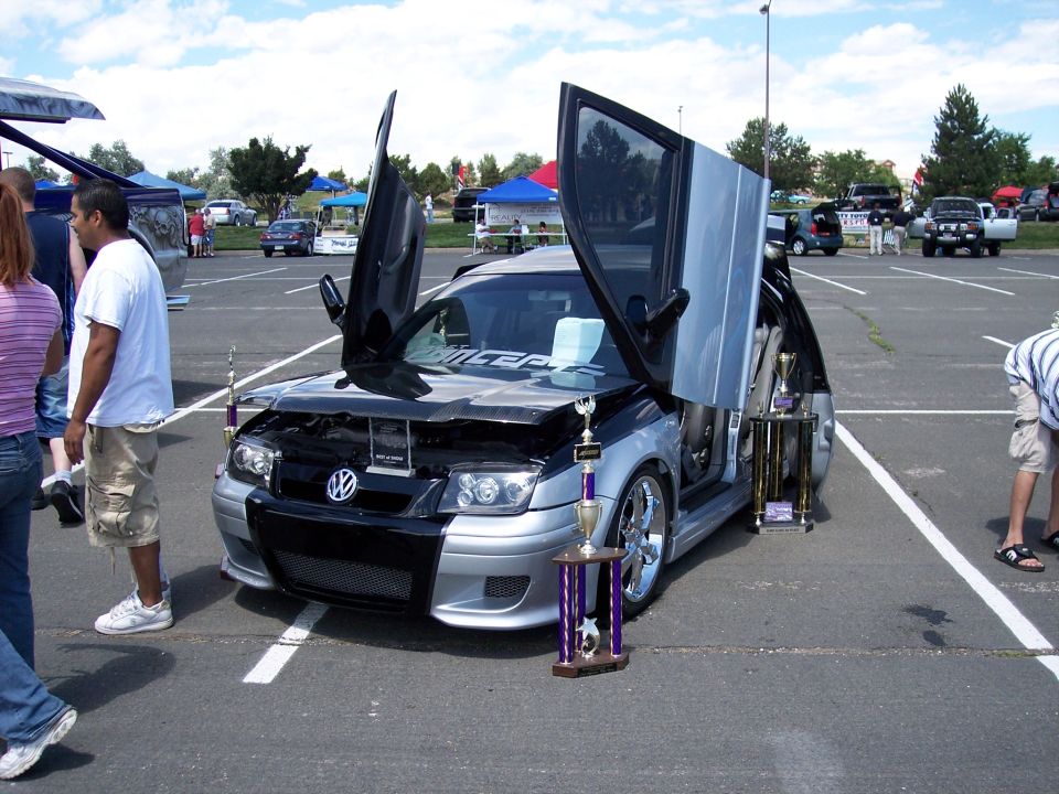 Silver and black Volkswagen Jetta with doors open, trophies on display