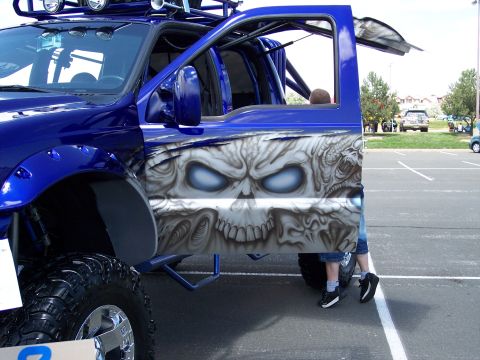 1972 Ford Ranchero - A custom blue pickup truck with a skull airbrushed on the door is parked in a lot.