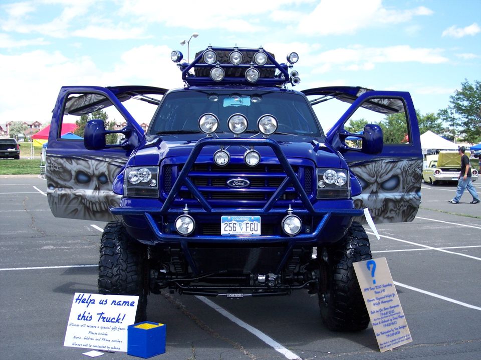 Blue Ford truck with open doors showing skull graphics, bull bar, and roof lights