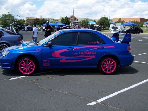 1972 Ford Ranchero - Blue Subaru WRX STI with pink racing stripes and pink wheels is parked in a lot with other vehicles.