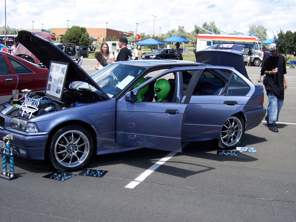 Blue sedan with doors open, an alien figure in the driver's seat. Hood is up showing the engine