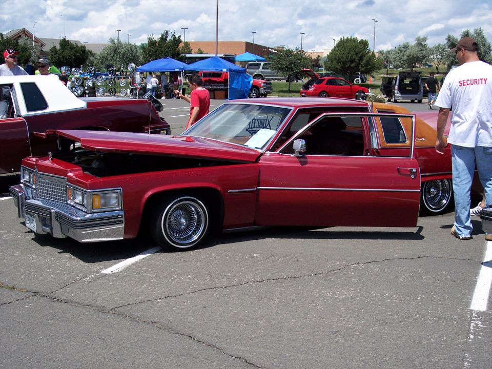 Red Cadillac sedan with hood and driver door open, wire wheels, vinyl top