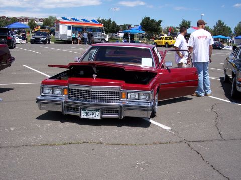 1972 Ford Ranchero - A red 1977 Cadillac Coupe DeVille is displayed with its hood and driver's door open at an outdoor event.