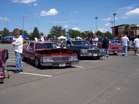 1972 Ford Ranchero - A red 1977 Cadillac Coupe de Ville is displayed with its hood up at a car show.