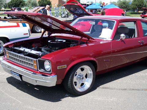 1972 Ford Ranchero - A bright red coupe with its hood open, revealing the engine and custom chrome wheels. The vehicle is parked outdoors at an event.