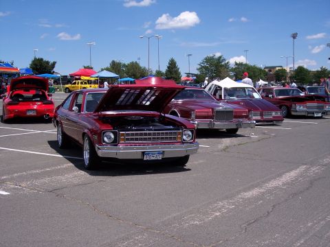 1972 Ford Ranchero - A red coupe with its hood open is parked in a lot with other vehicles under a bright blue sky.