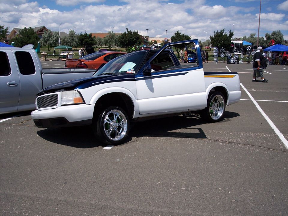 White pickup truck with blue accents and chrome wheels parked at an outdoor event