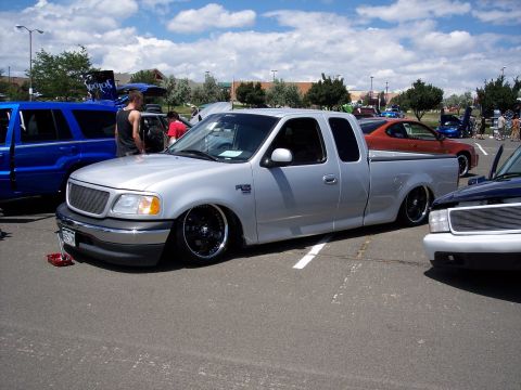 1972 Ford Ranchero - A silver pickup truck with custom wheels sits low to the ground at an outdoor event.