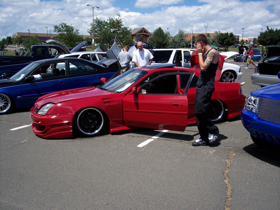 Red sports coupe with doors open, parked at a car show. A guy stands next to it