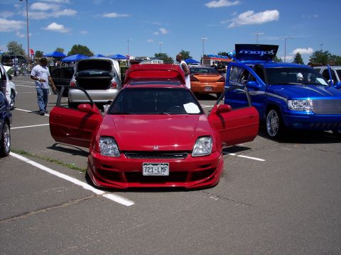 1972 Ford Ranchero - Red Honda Prelude on display at a car show, with multiple other vehicles present under a sunny sky.