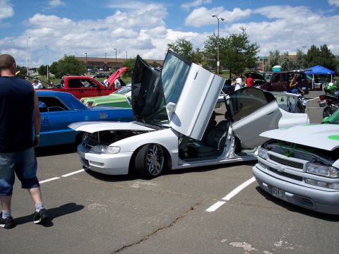 1972 Ford Ranchero - A white sedan with its doors open, displayed at an outdoor car show with other vehicles present.