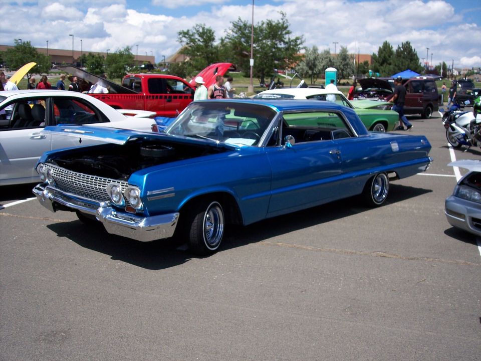 Blue 1963 Chevrolet Impala coupe with hood open, parked at an outdoor car show