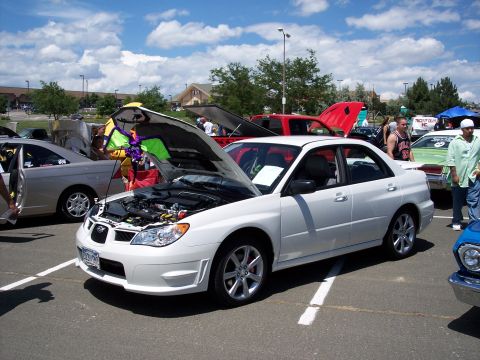 1972 Ford Ranchero - A white Subaru Impreza WRX is displayed with its hood open at a car show, surrounded by other vehicles.