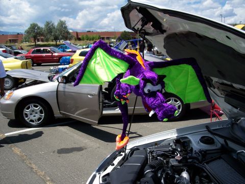 1972 Ford Ranchero - A plush purple dragon hangs from the open hood of a silver car at an outdoor event.