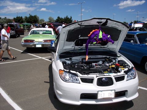 1972 Ford Ranchero - A white Subaru Impreza WRX is displayed with its hood open, revealing the engine and a purple dragon toy hanging from the latch.