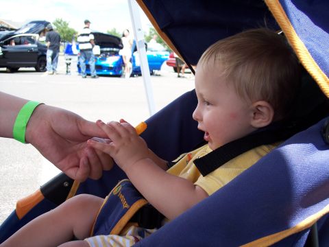 1972 Ford Ranchero - A child in a stroller looks on as an adult's hand reaches towards them, with cars visible in the background.