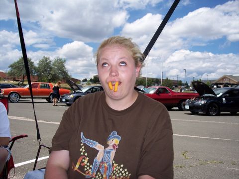 1972 Ford Ranchero - A woman with cheese puffs in her mouth looks upwards at a car show.