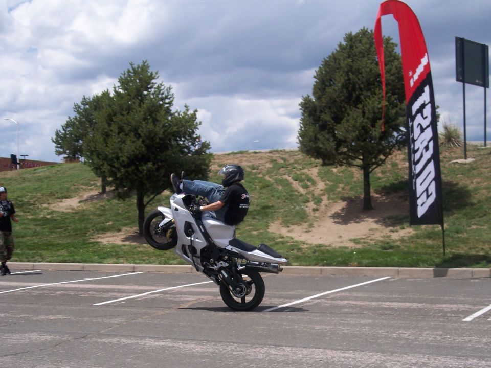 White sportbike doing a wheelie in a parking lot with a red and black flag in the background