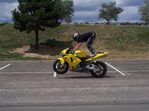 1972 Ford Ranchero - A person performs a stunt on a yellow motorcycle, lifting the front wheel off the ground.