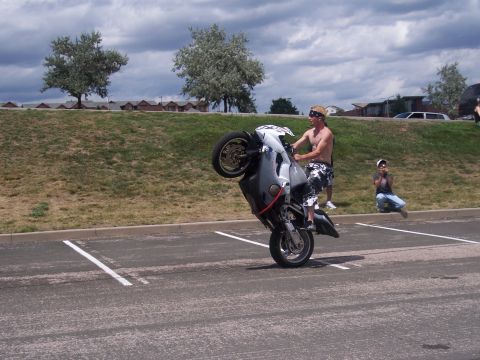 1972 Ford Ranchero - A rider performs a wheelie on a motorcycle in a parking lot, with spectators watching.