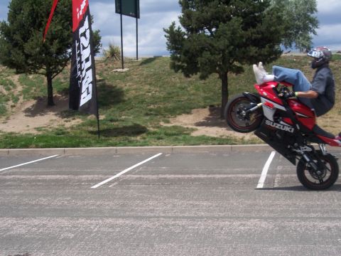1972 Ford Ranchero - A rider performs a wheelie on a Suzuki motorcycle in a parking lot, with a promotional flag nearby.
