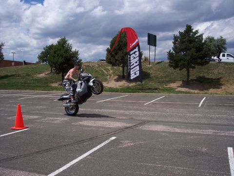 1972 Ford Ranchero - A motorcycle is performing a wheelie in a parking lot, with a large banner and trees in the background.