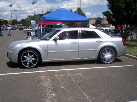 1972 Ford Ranchero - A silver sedan with custom chrome wheels is parked outdoors under a blue tent.