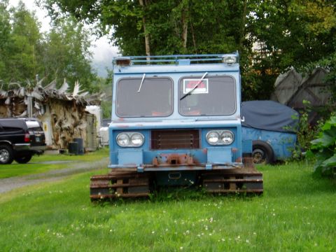 2000 Ford E350 - A blue tracked vehicle sits on a grassy area, with another vehicle covered in a blue tarp in the background.