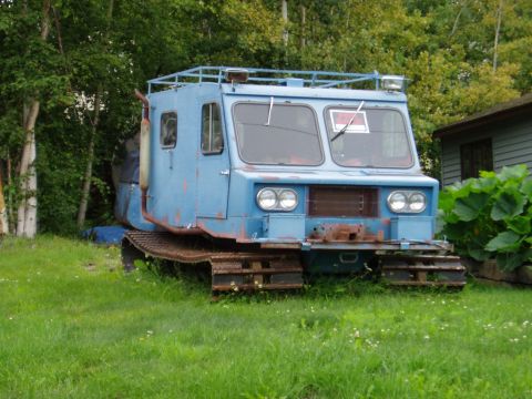 2000 Ford E350 - A blue tracked vehicle sits parked on a grassy area next to trees and a building.