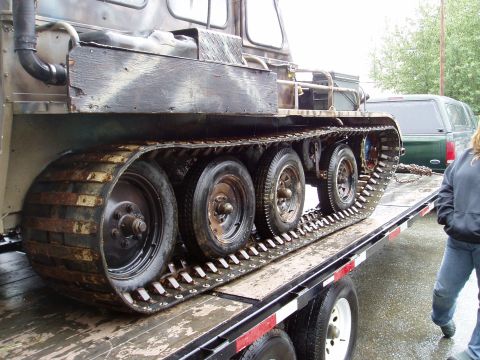 2000 Ford E350 - A unique tracked vehicle is transported on a trailer, with a green SUV visible in the background.