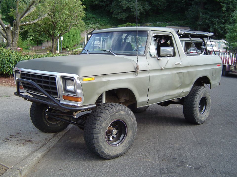 Lifted tan Ford Bronco with top off and tube brush guard, front 3/4 view on a street