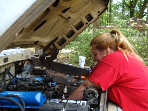 1967 Ford F-250 - A person works on the engine of a vehicle with the hood open, surrounded by trees.