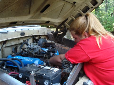 1967 Ford F-250 - A person works on the engine of a 1967 Ford F-250, with the hood open and the engine bay visible.