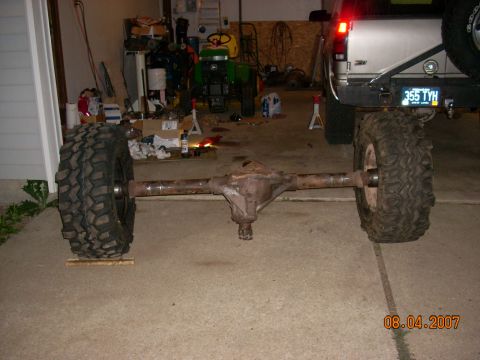 2000 Chevrolet Tahoe - A detached rear axle assembly with large tires is displayed in a garage setting, with a vehicle in the background.
