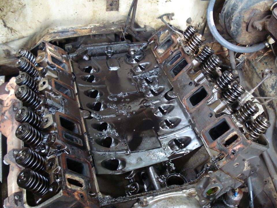 Engine block with intake and exhaust ports visible, showing valves and valve springs. Oil is present