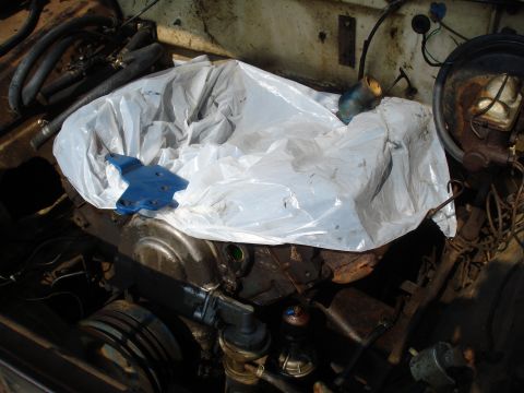 1967 Ford F-250 - Engine bay view with a plastic bag draped over the engine. A blue bracket is visible on top.