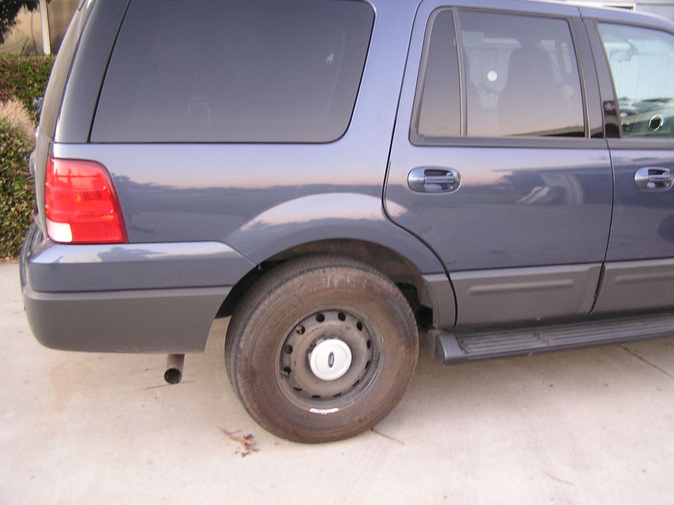 Rear quarter of a dark blue Ford SUV showing steel wheel, taillight and running board on a concrete driveway
