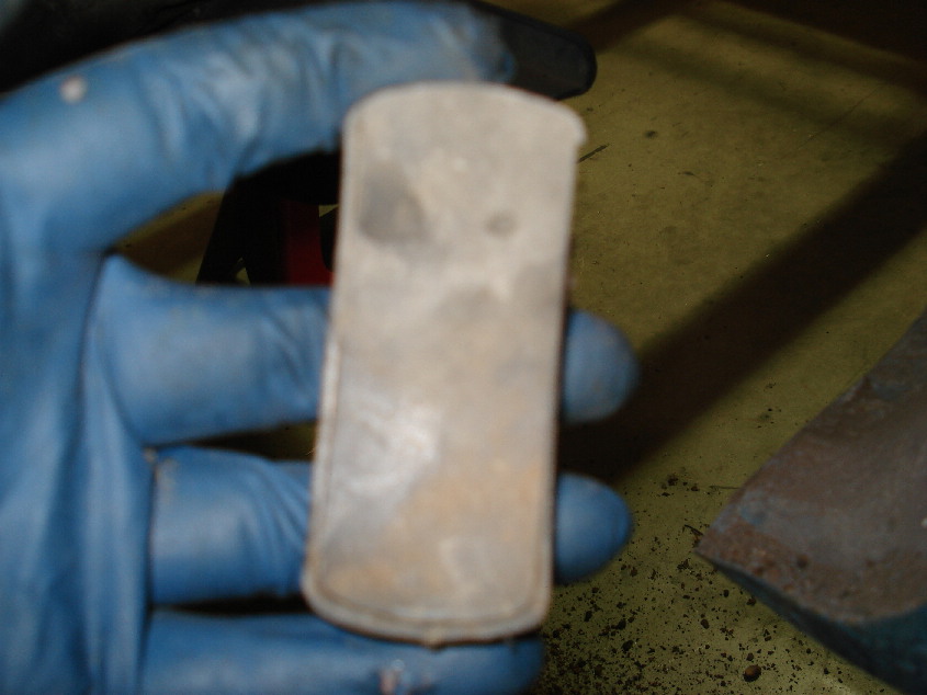 Blue-gloved hand holding a small worn metal bushing or bearing shell over a workbench