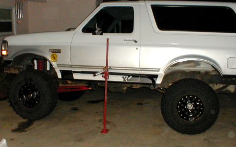 1996 Ford Bronco - This white Ford Bronco is being worked on, with a jack lifting one side to show the suspension and large tires.