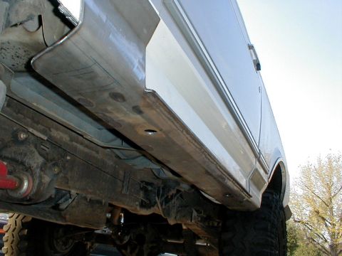 1996 Ford Bronco - Custom metal rock sliders are being installed on the side of a vehicle, viewed from below.