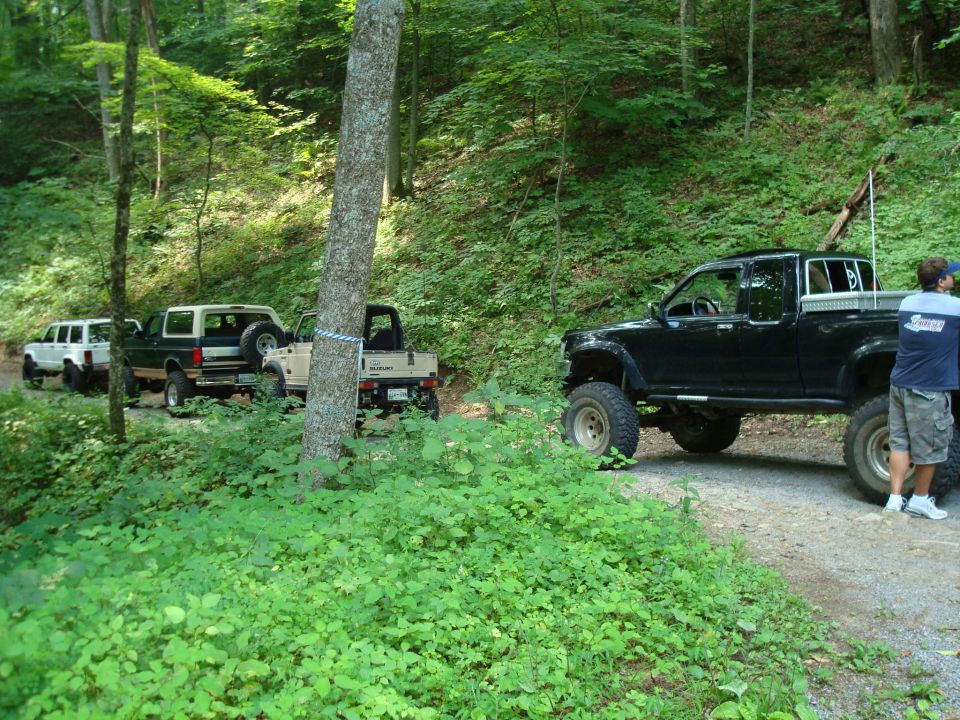 Tan 1992 Ford Bronco with a white top and spare tire on the back, parked on a dirt road