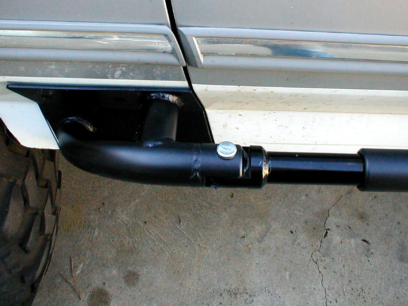 Close-up of a black metal rock slider attached to the side of a vehicle, with a tire visible on the left