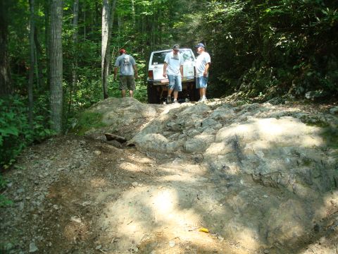 1995 Ford Bronco - Three people stand behind a white 1995 Ford Bronco on a challenging rocky trail.
