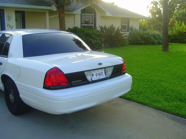 Rear view of white 2003 Ford Crown Victoria parked in driveway, house and lawn in background