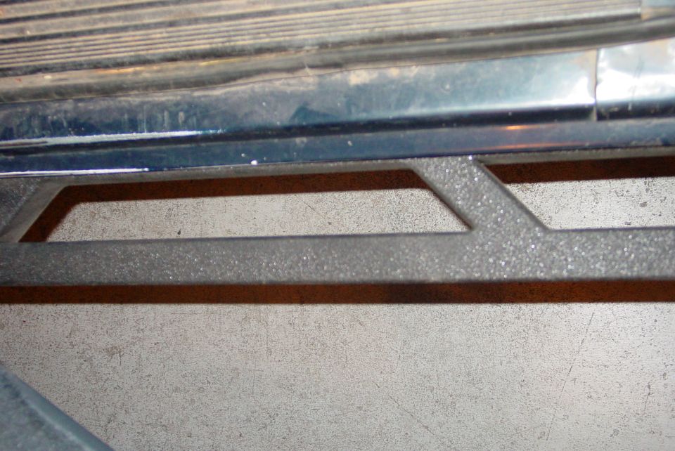 Close-up of a textured running board on a dark-colored vehicle, with the ground visible below